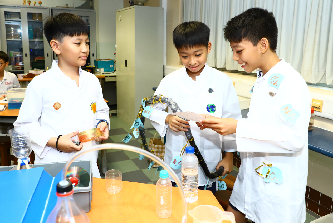 A smiling female teacher guides several students around a table with colorful liquids in beakers during a science class.